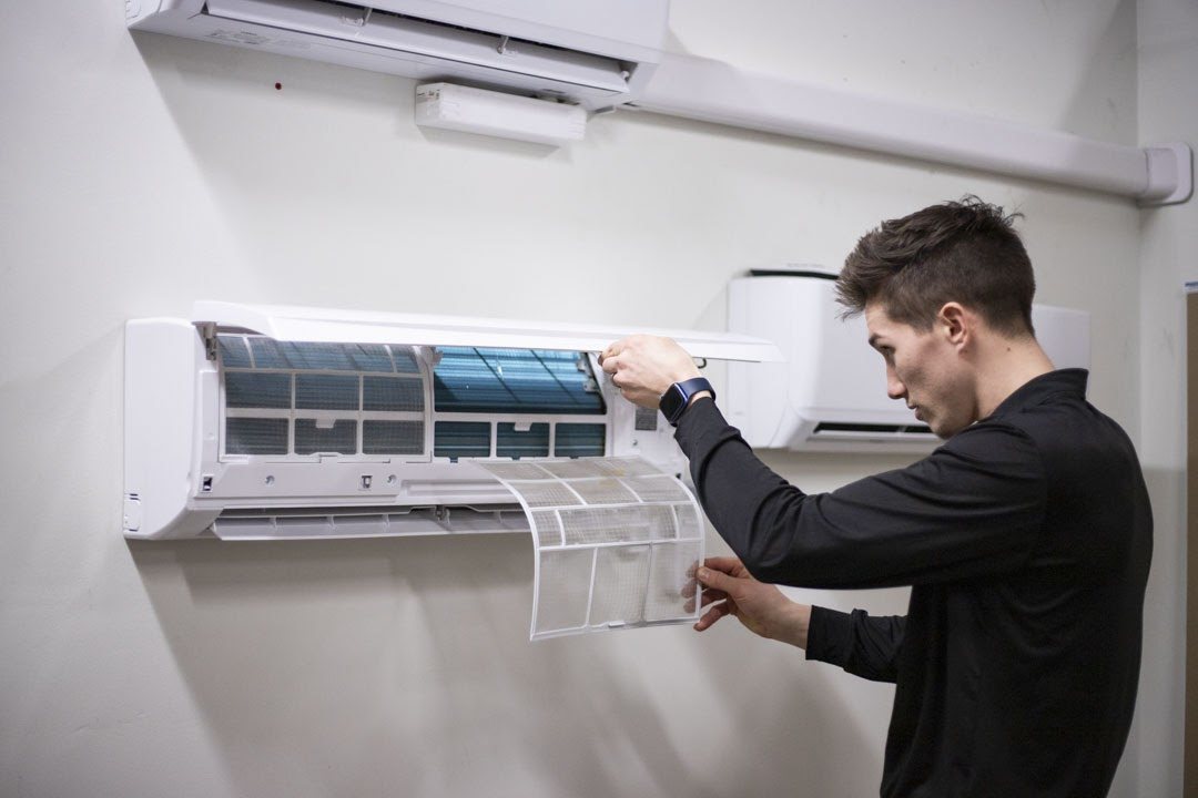 Technician lifting the front panel and filter of a wall-mounted mini-split indoor unit for cleaning