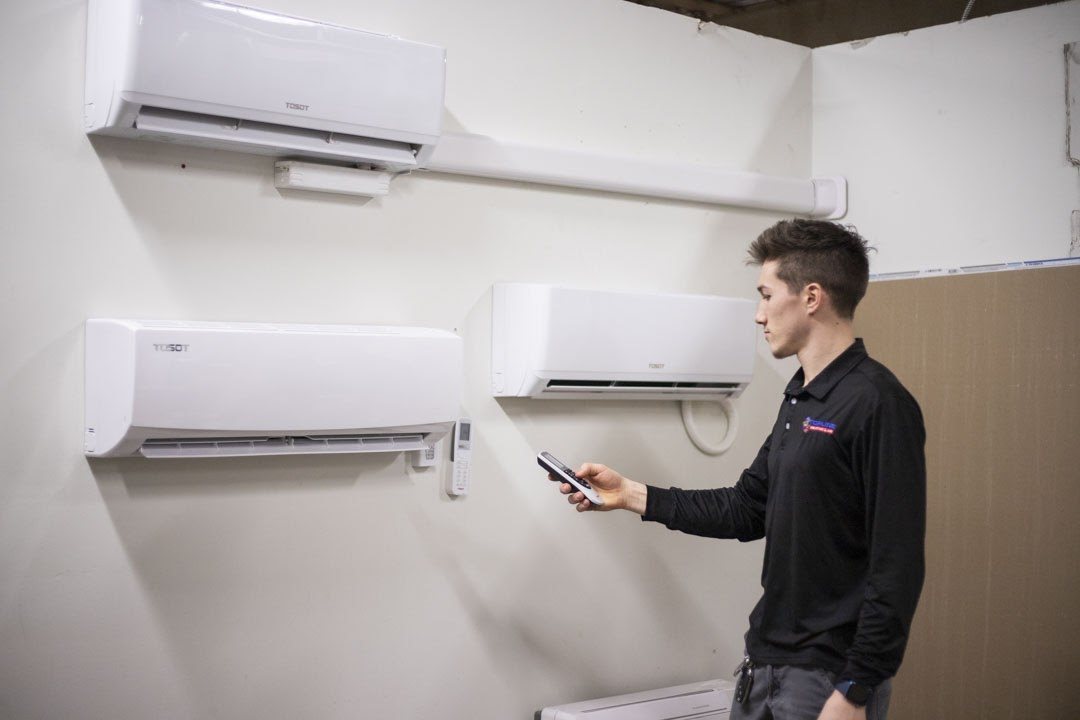 Topline technician using a remote to control wall-mounted ductless mini-split indoor units