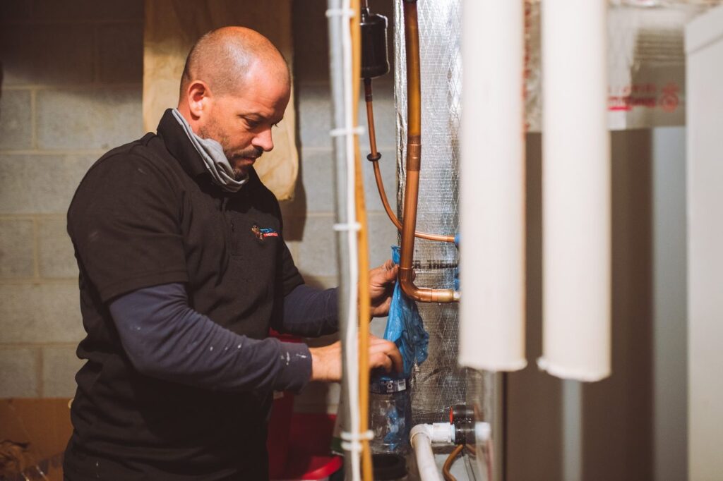Topline technician working on copper refrigerant lines and venting beside a newly installed furnace in a basement